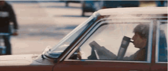 a man is reading a book while driving a car on a city street .