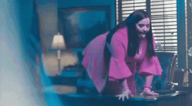 a woman in a pink dress is kneeling on a desk in a living room .