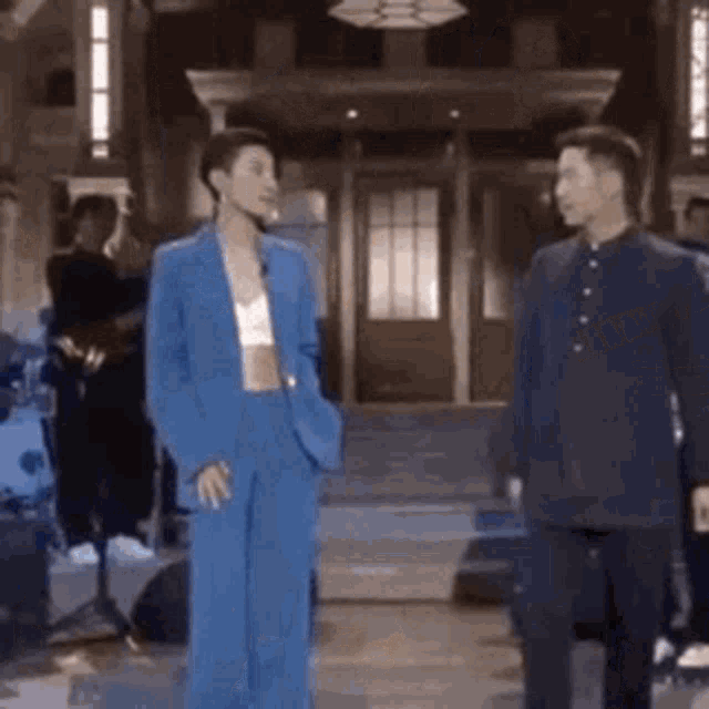 a man and a woman are standing next to each other in a room . the woman is wearing a blue suit .