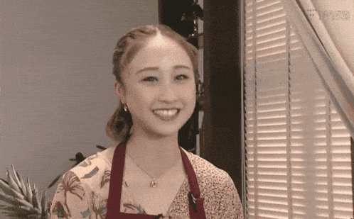 a woman wearing an apron is smiling in front of a window with blinds