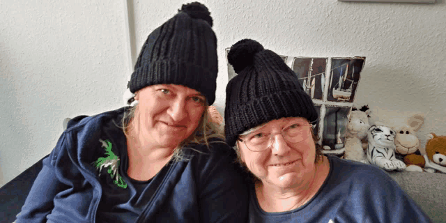 two women wearing black beanies are sitting on a couch