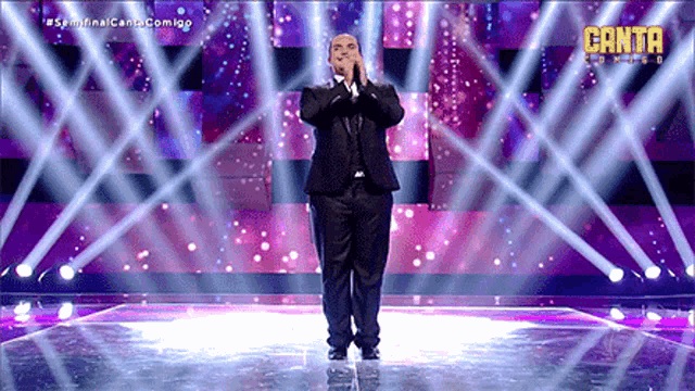 a man in a suit stands on a stage in front of a canta logo