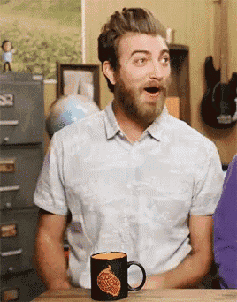 a man with a beard is sitting at a table with a coffee mug with a flame on it .