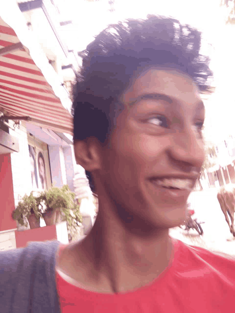 a man in a red shirt is smiling in front of a store