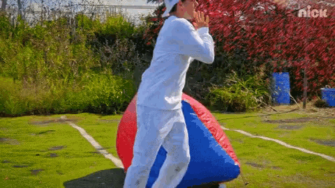 a man in a white shirt is standing next to a red and blue ball with the nick logo on the bottom