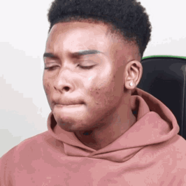 a young man in a pink hoodie is making a funny face with his eyes closed