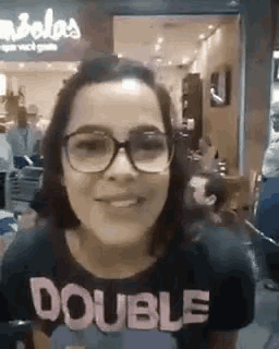 a woman wearing glasses and a black shirt with the word double on it .