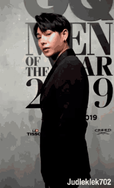 a man in a suit stands in front of a wall that says men of the year 2019