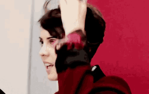 a woman with a tattoo on her arm is holding her hair up in front of a red wall .