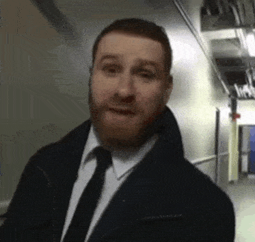 a man with a beard and tie is standing in a hallway and making a funny face .