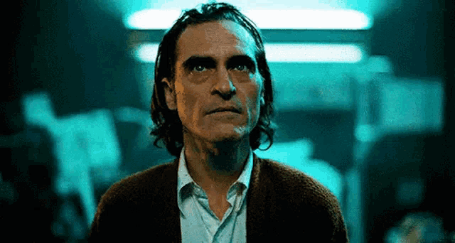 a man with long hair and a beard is standing in a dark room and looking at the camera .