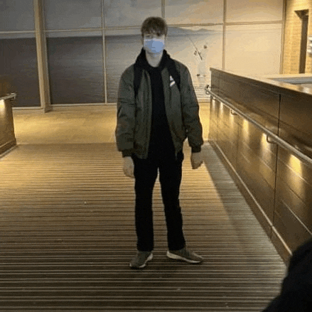 a young man wearing a mask and a bomber jacket is standing on a wooden floor .