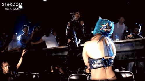 a woman in a blue mask stands in front of a crowd with the word stardom on the bottom