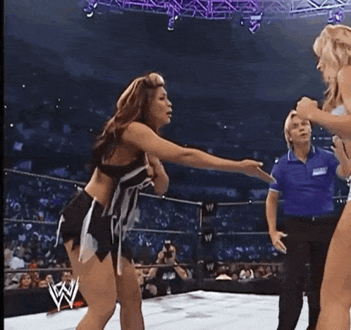 two women are fighting in a wrestling ring with a referee watching .
