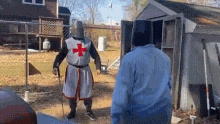 a man dressed as a knight with a red cross on his chest is standing next to another man .