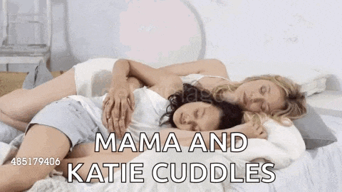 two women are laying on a bed hugging each other and the caption says mama and katie cuddles .