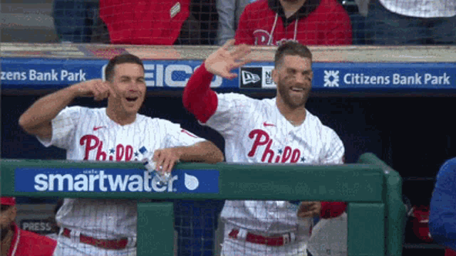 two philadelphia phillies baseball players are waving from the dugout