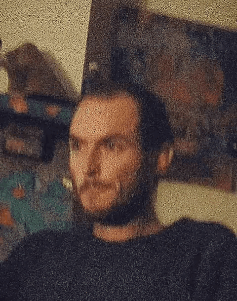 a man with a beard is sitting in front of a painting on the wall