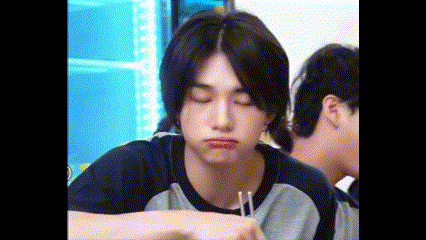 a young man is sitting at a table with chopsticks in his hand and making a funny face .