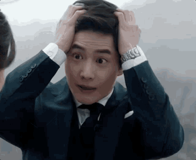 a man in a suit and tie is holding his head in his hands .
