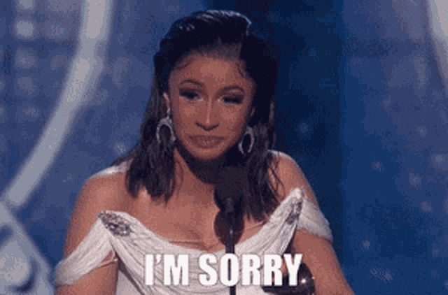 a woman in a white dress is standing in front of a microphone and saying i 'm sorry