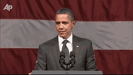 a man in a suit and tie is giving a speech in front of a flag with the letters ap on it