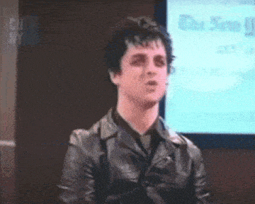 a man in a leather jacket is sitting in front of a tv screen that says the new york times