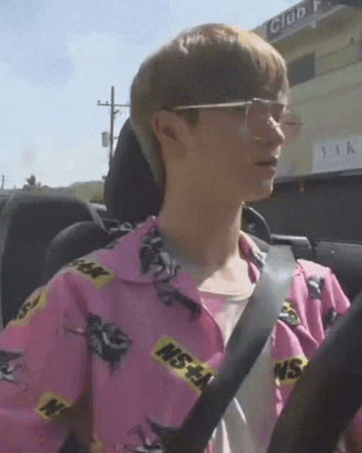 a man wearing glasses and a pink shirt with the word ns on it