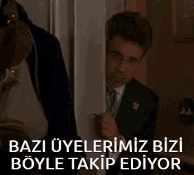 a man in a suit and tie peeking out from behind a door with the words bazi uyelerimiz bizi böyle takip ediyor