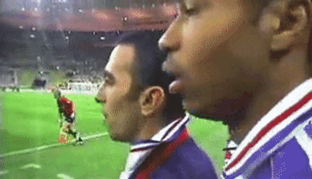 two men are standing on a soccer field and one of them is talking to the other .