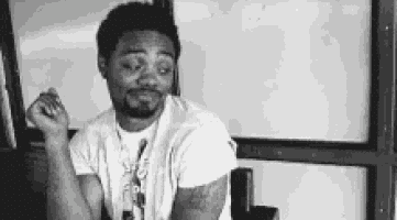 a black and white photo of a man sitting in front of a white board .