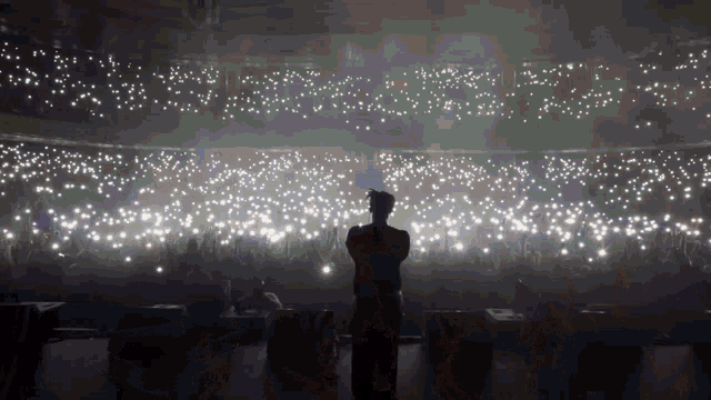 a man stands on a stage in front of a crowd of people holding their cell phones up