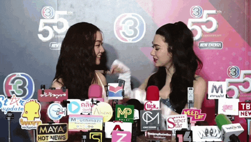 two women are talking in front of a wall that has the number 55 on it