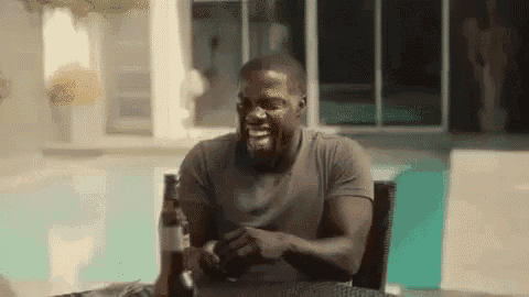 a man is sitting at a table with a bottle of beer and laughing .