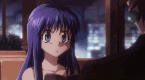 a girl with purple hair and blue eyes is sitting next to a man in a dark room .