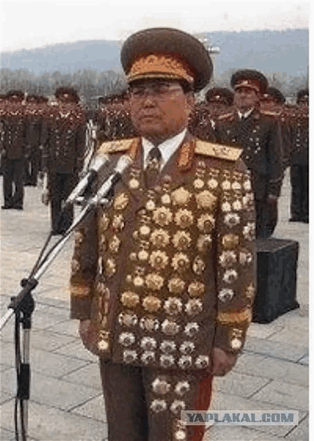 a man in a military uniform is standing in front of a microphone in front of a row of soldiers .