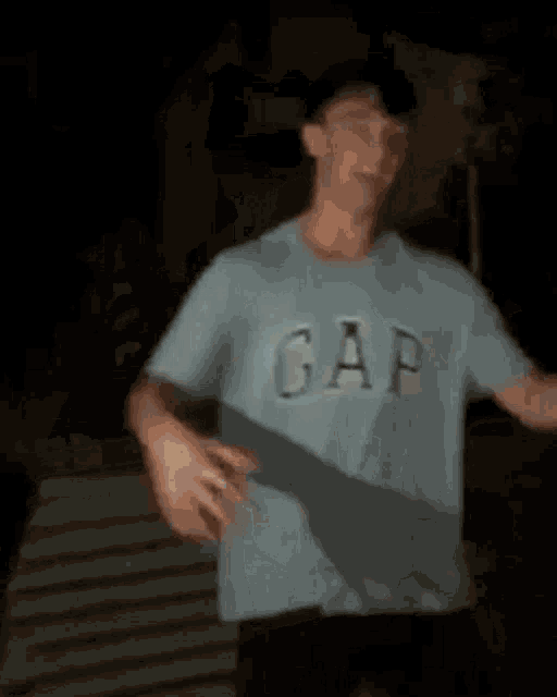 a man wearing a gap t-shirt is standing in a dark room .