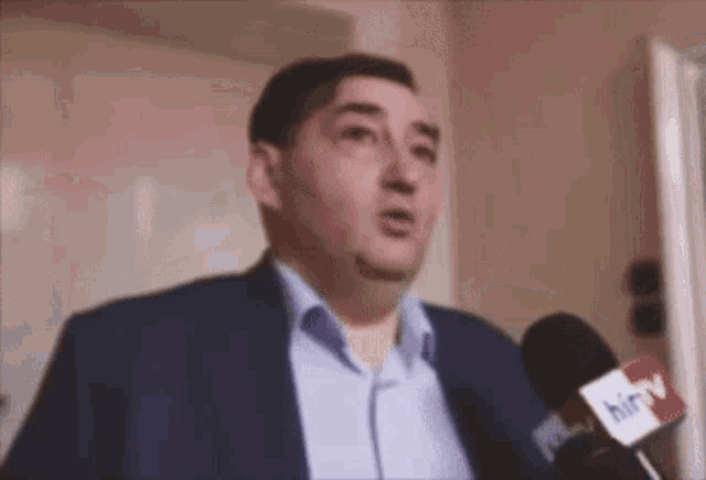 a man in a suit is talking into a microphone with the word hirv on it .