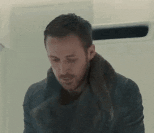 a man with a beard and a scarf around his neck is standing in front of a wall .