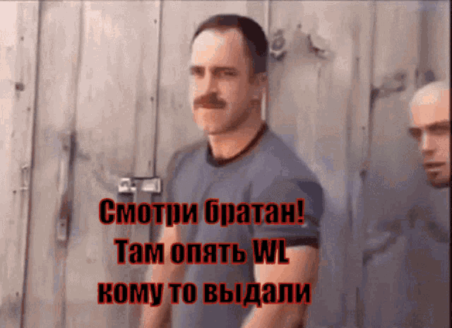 a man with a mustache is standing in front of a wooden wall with the words " смотри братан " on it