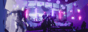 a group of people are dancing in a room with purple lights and balloons
