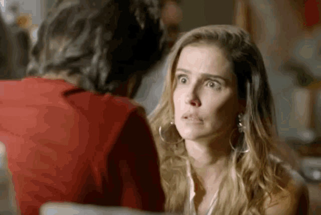 a woman is making a funny face while looking at a man in a red shirt