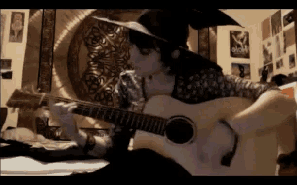 a person playing an acoustic guitar in a room with posters on the wall including one that says " hope "