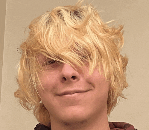a young man with blonde hair and a mustache looks at the camera