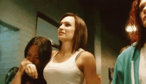 a woman in a white tank top is standing next to two other women in a dark room .