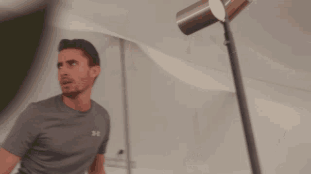 a man wearing a grey under armour shirt is standing in front of a lamp