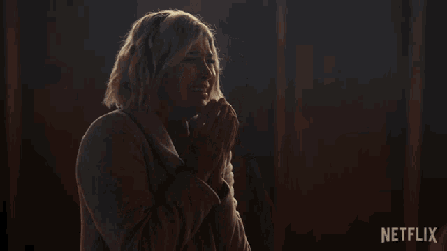 a woman is holding her head in a dark room with a netflix logo in the corner