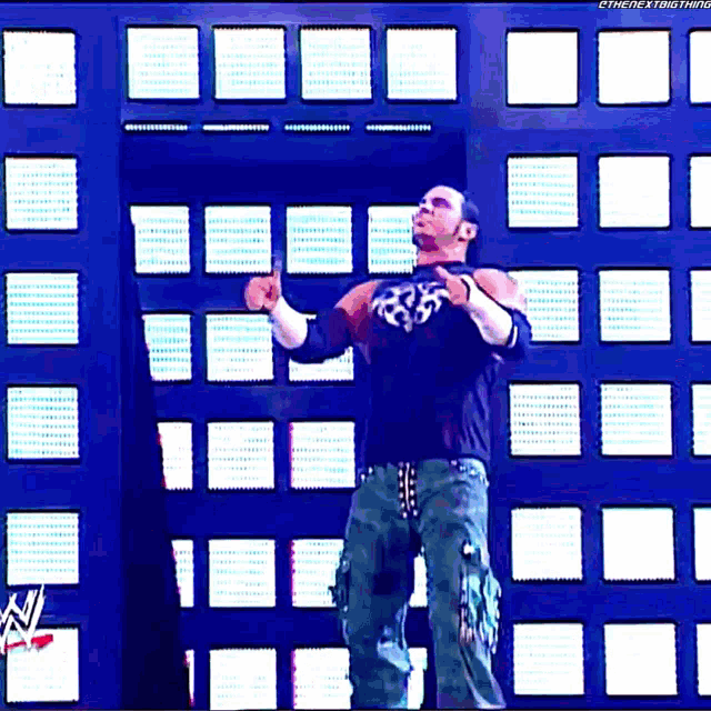 a wrestler is standing in front of a wall with a watermark that says " the next thing "