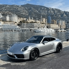a silver porsche 911 carrera s is parked on the side of the road next to a body of water .
