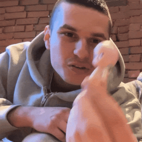 a man in a grey hoodie holds a white object in front of his face